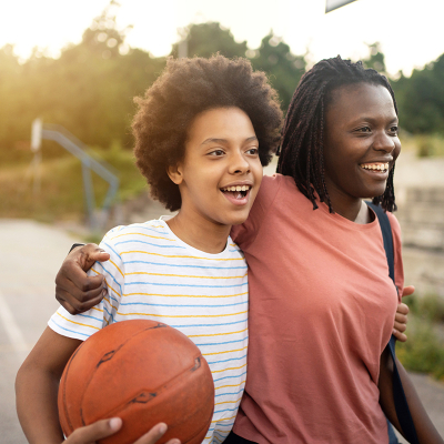 Two friends with their arms around each other, holding a basketball. 