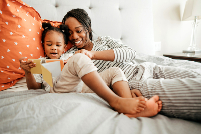 A woman and young child reading a book in bed