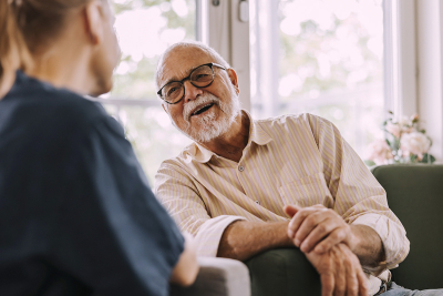 Elderly man sitting in a chair smiling at a person