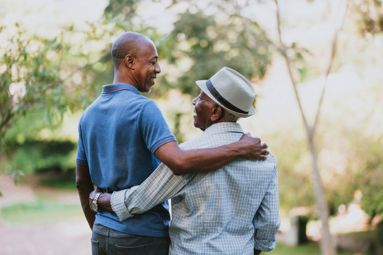 An older man and his son holding each other and smiling at each other